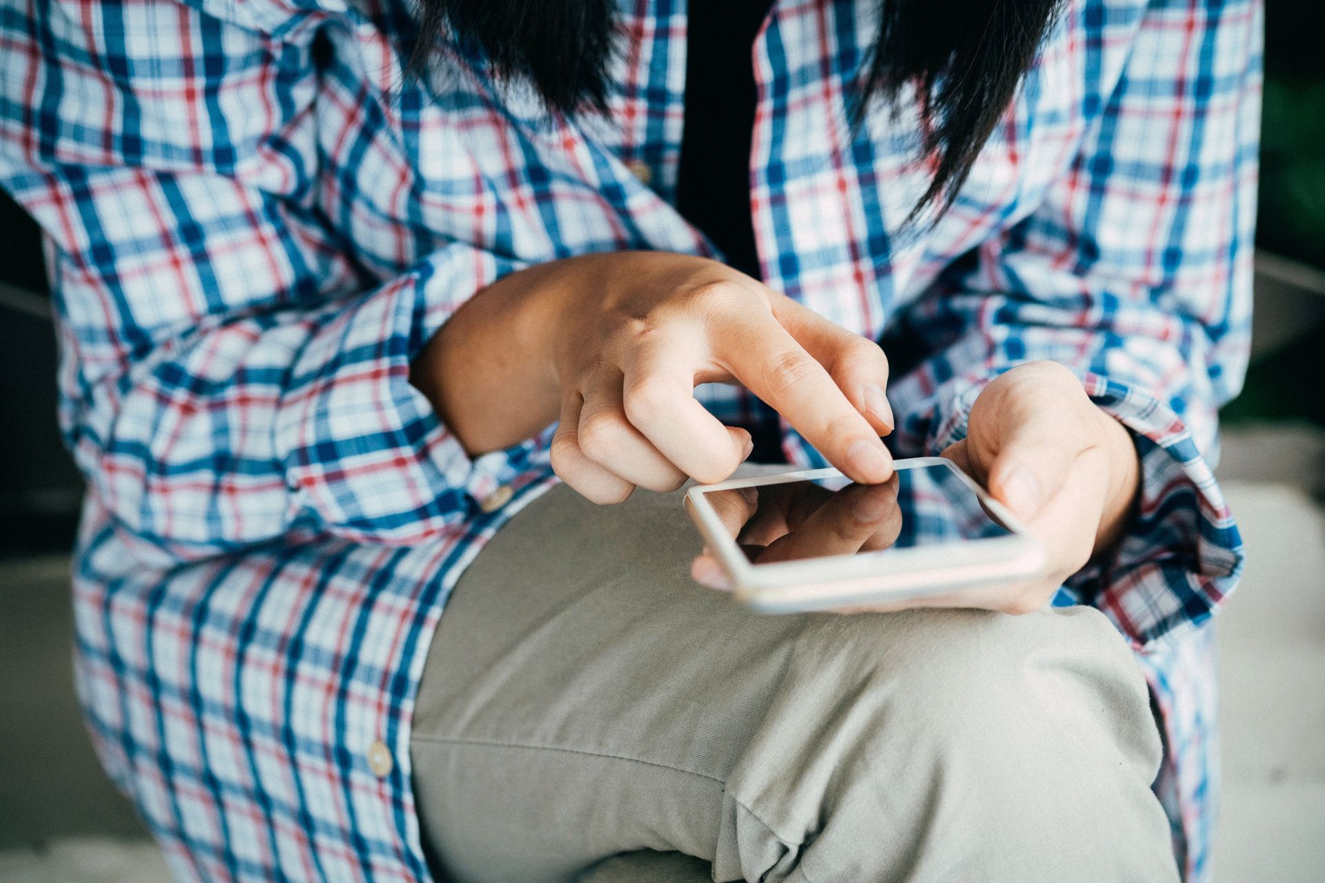 A woman in a plaid shirt is sitting down using a cell phone.