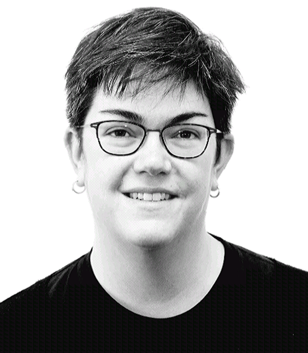 A woman wearing glasses and earrings is smiling in a black and white photo.