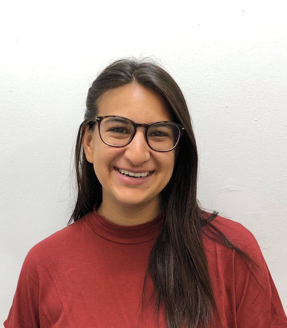 Une femme portant des lunettes et une chemise rouge sourit à la caméra.