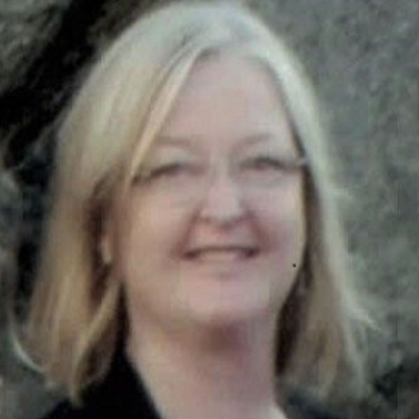 Une femme aux cheveux blonds et aux lunettes sourit à la caméra.