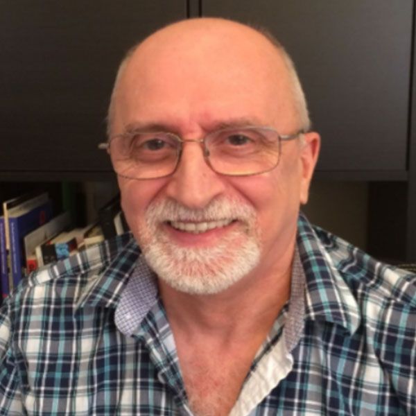 Un homme chauve avec des lunettes et une barbe sourit à la caméra.