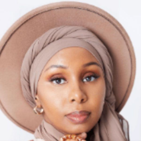 Une femme portant un chapeau et une écharpe regarde la caméra