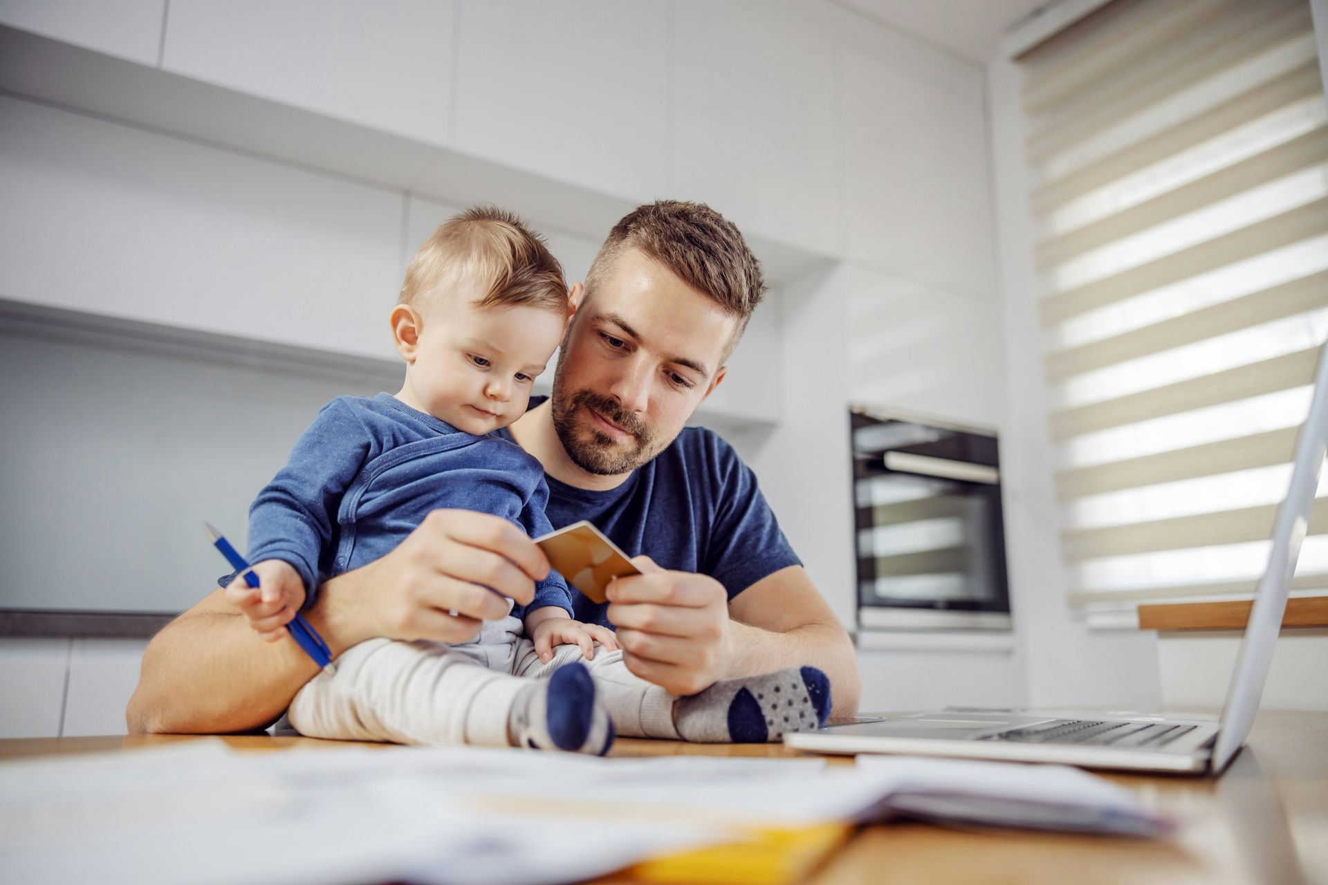 A father holding his baby and reviewing a credit card, symbolizing life insurance quotes and personalized life insurance options for families.