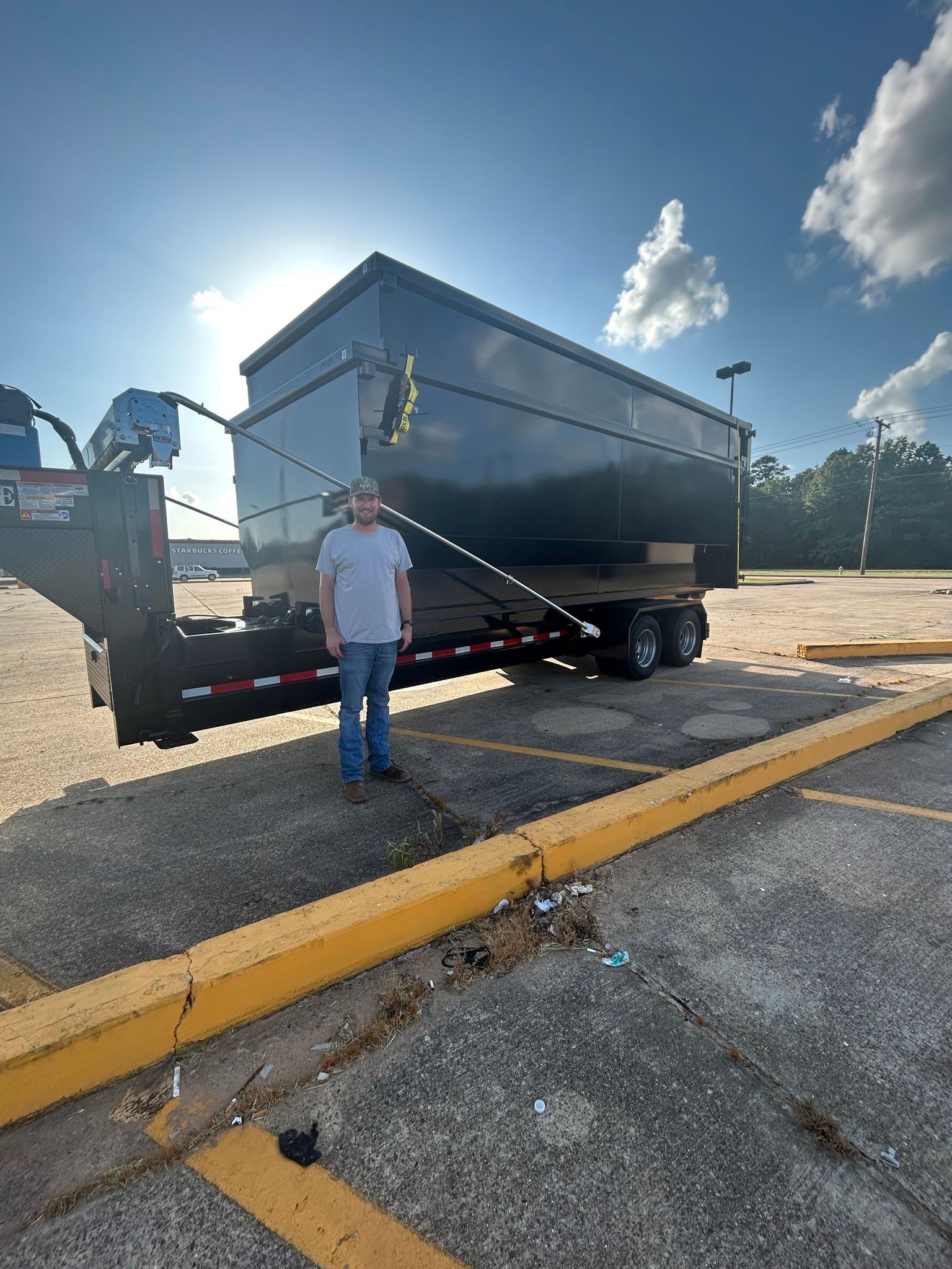 A man is standing in front of a dumpster trailer in a parking lot.