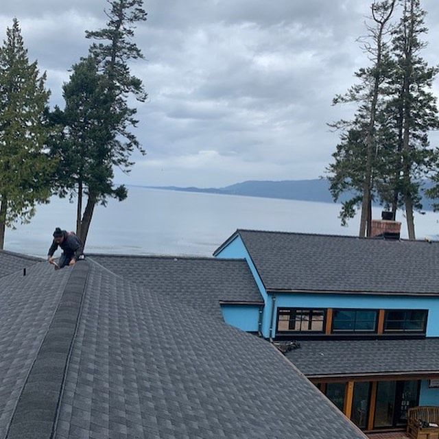 A man is working on the roof of a house overlooking a body of water