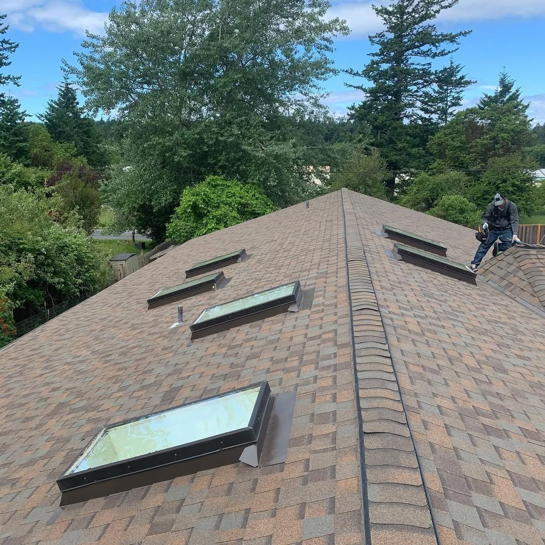 A man is standing on top of a roof with skylights.