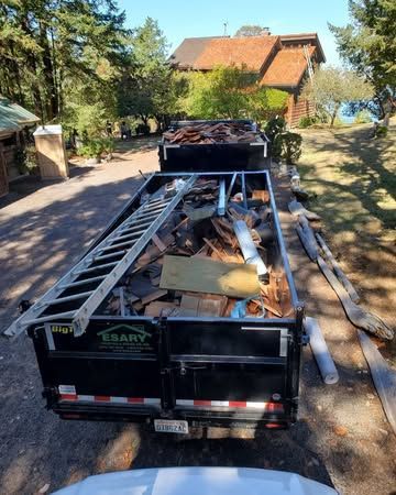A dumpster filled with junk is parked in front of a house.