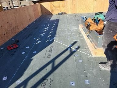 A man is standing on a roof with a bag of tools.
