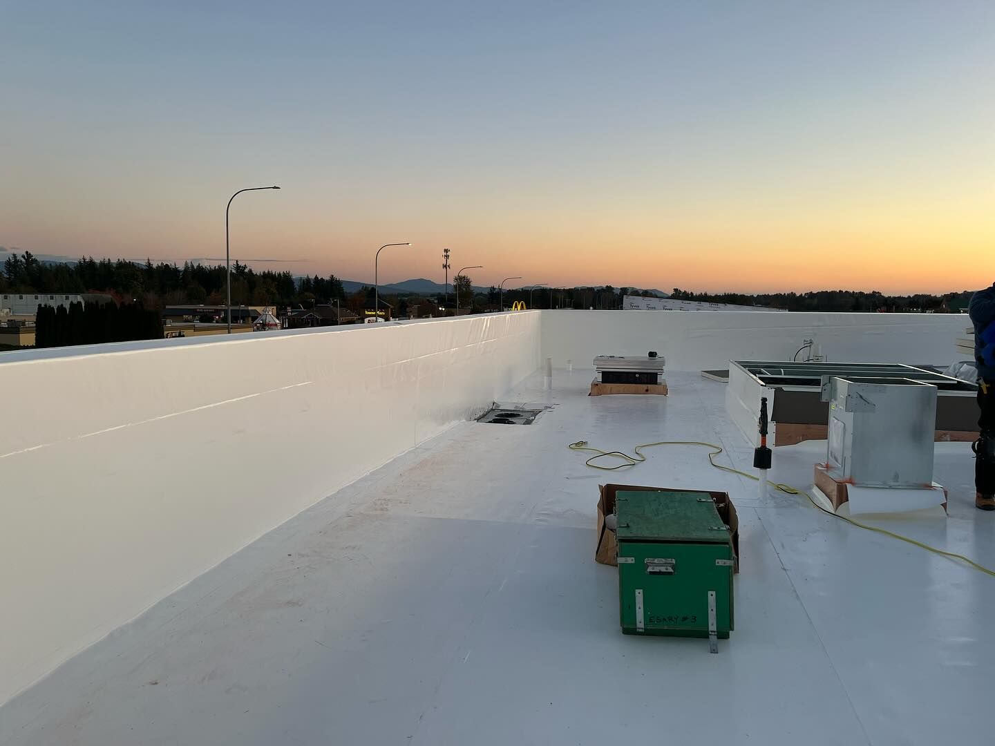 A man is working on a white roof at sunset.