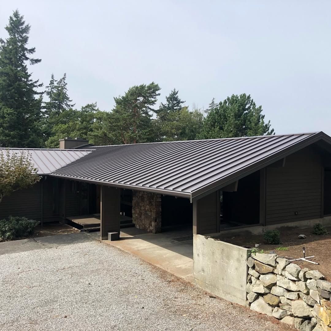 A house with a metal roof is surrounded by trees and gravel.