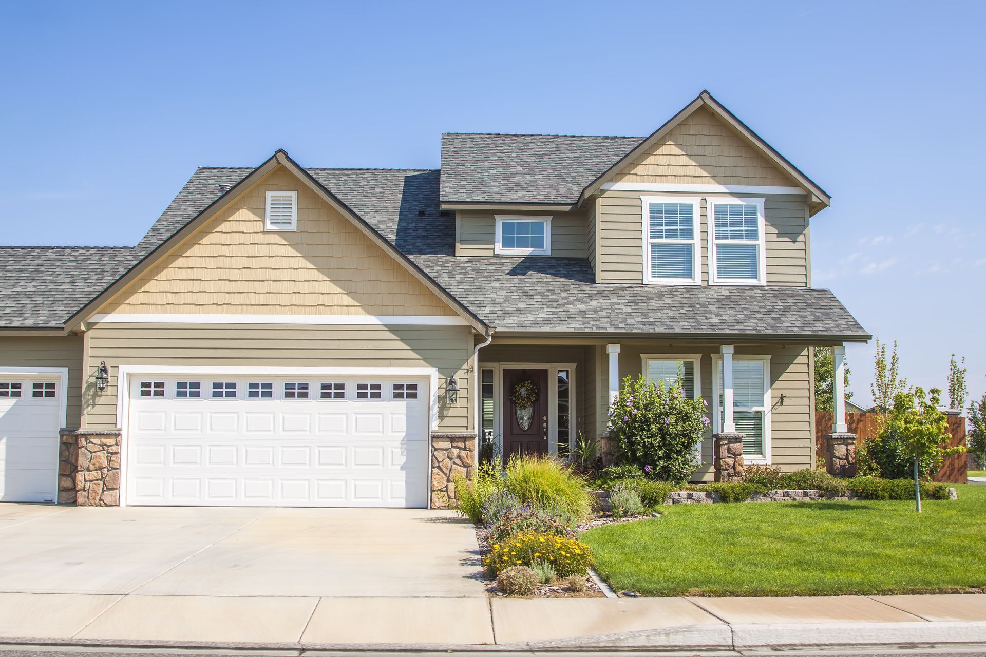 A large house with two garage doors and a lush green lawn.
