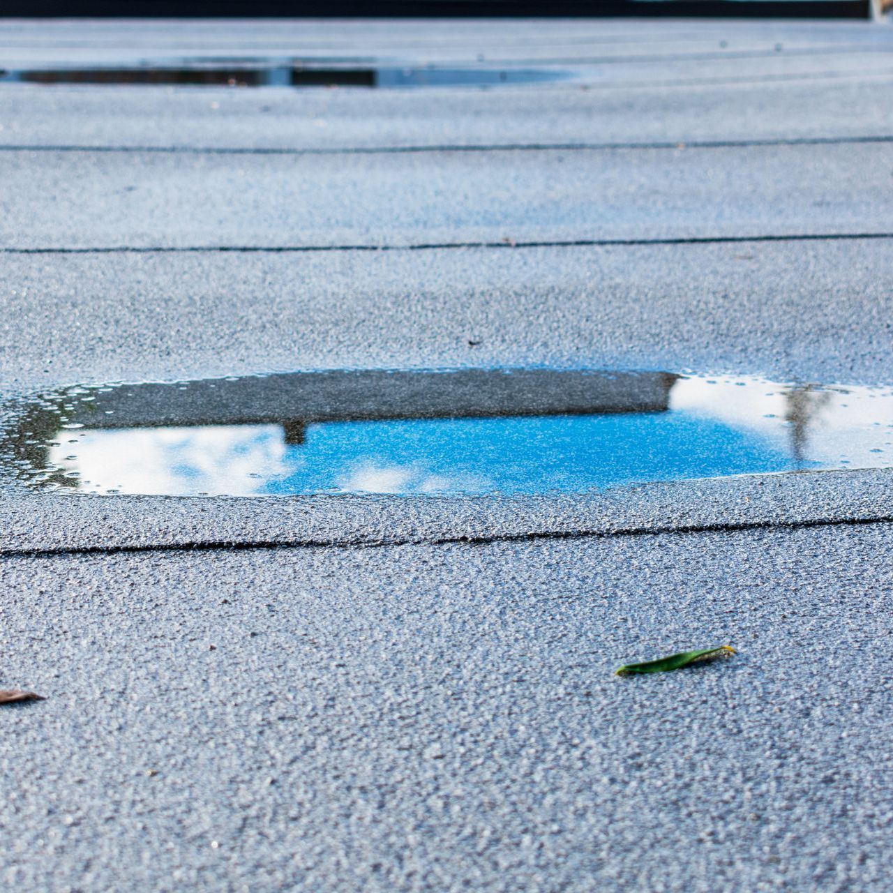 A close up of ponding water on a flat roof with a reflection of the sky in it.