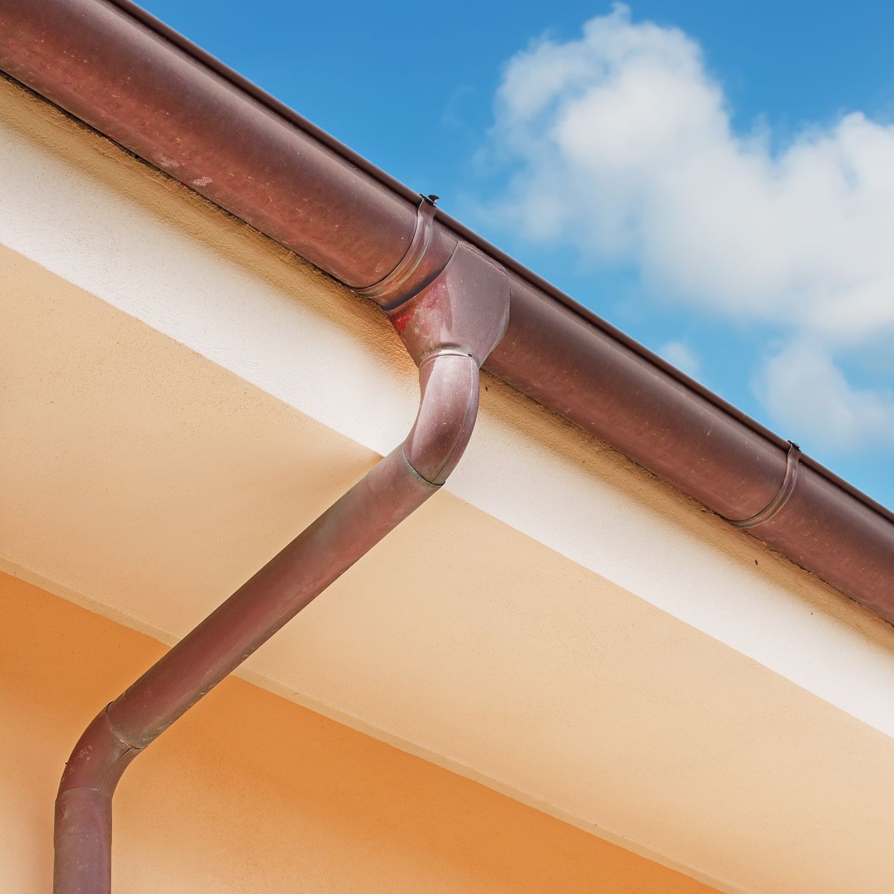 A close up of a copper gutter on the roof of a house with a blue sky in the background.