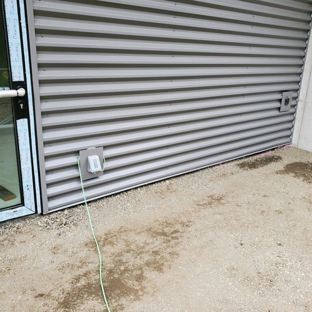 A closeup of a building with custom siding and a green cord is plugged into the wall next to a door 