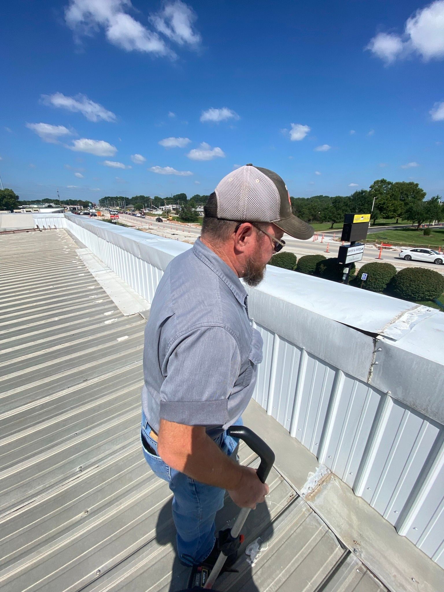 Man on a rooftop inspecting a white metal roof under a clear blue sky