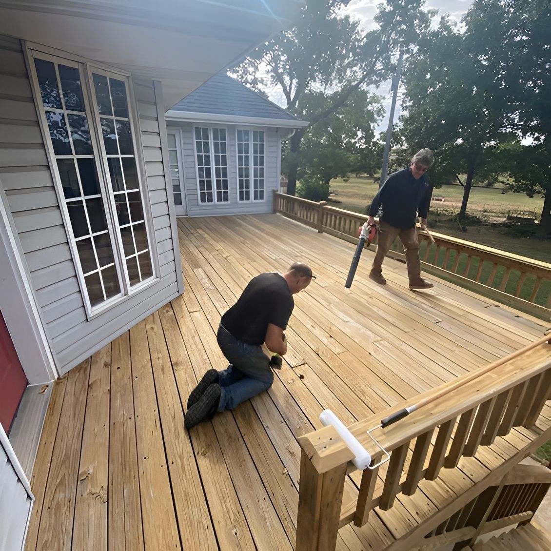 Two people installing a wooden deck beside a house on a sunny day.