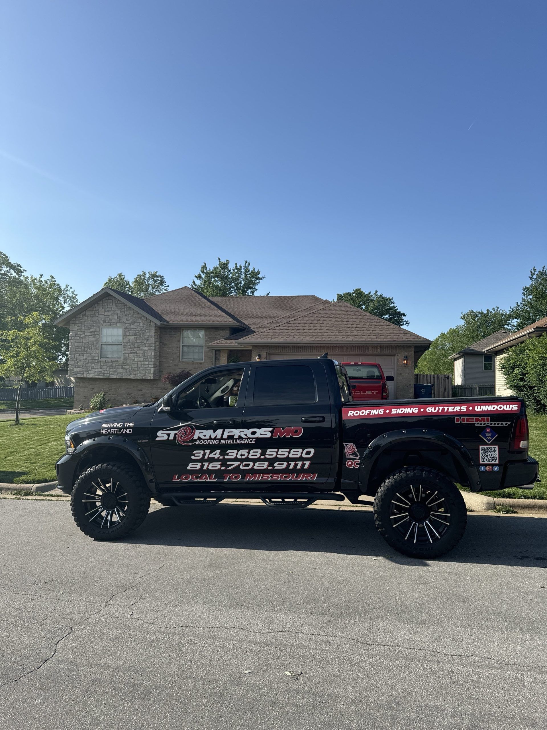 Black lifted pickup truck with company decals parked on a suburban street under a clear blue sky