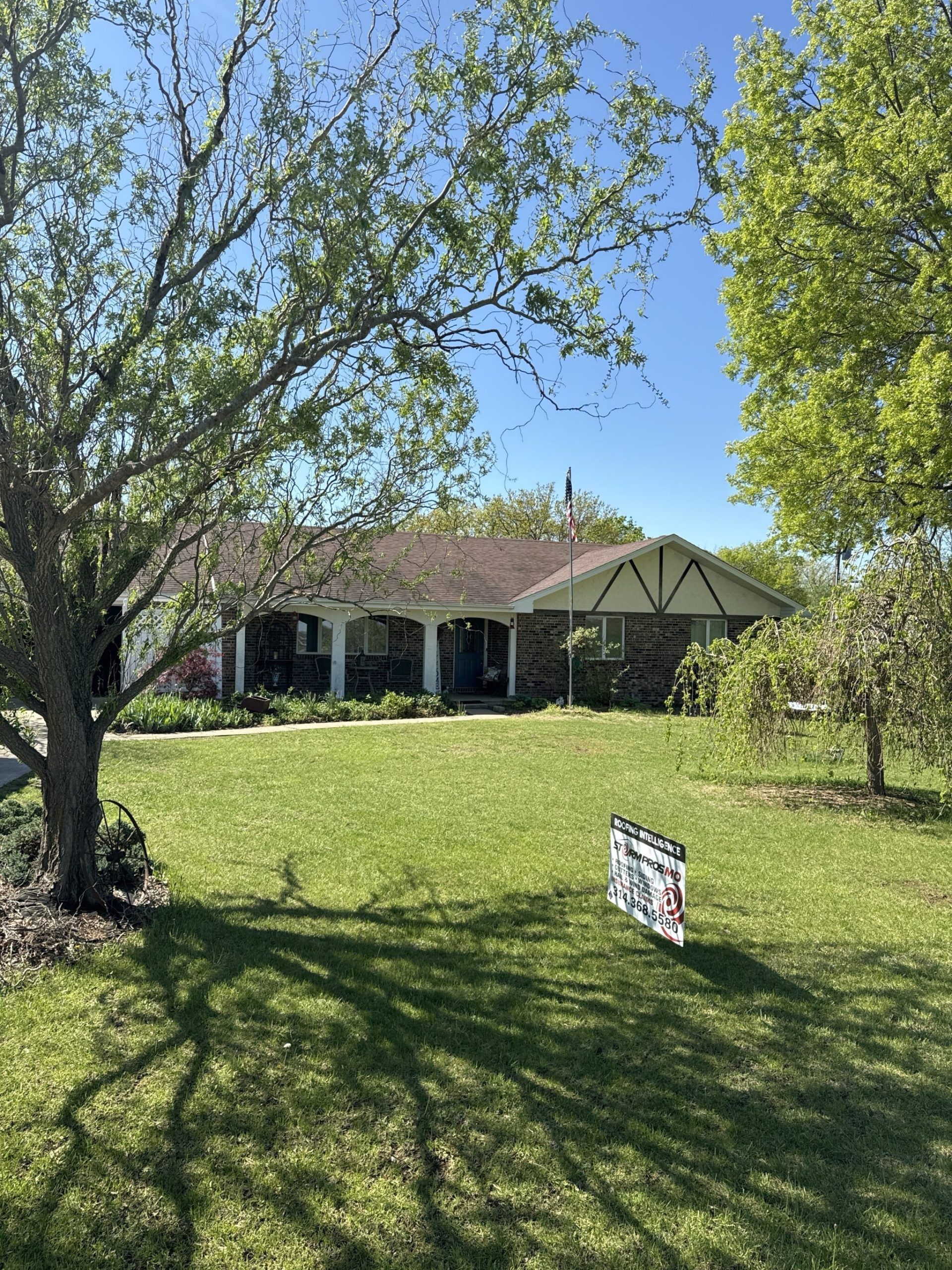 Suburban house with a green lawn, trees, and a small yard sign in the foreground