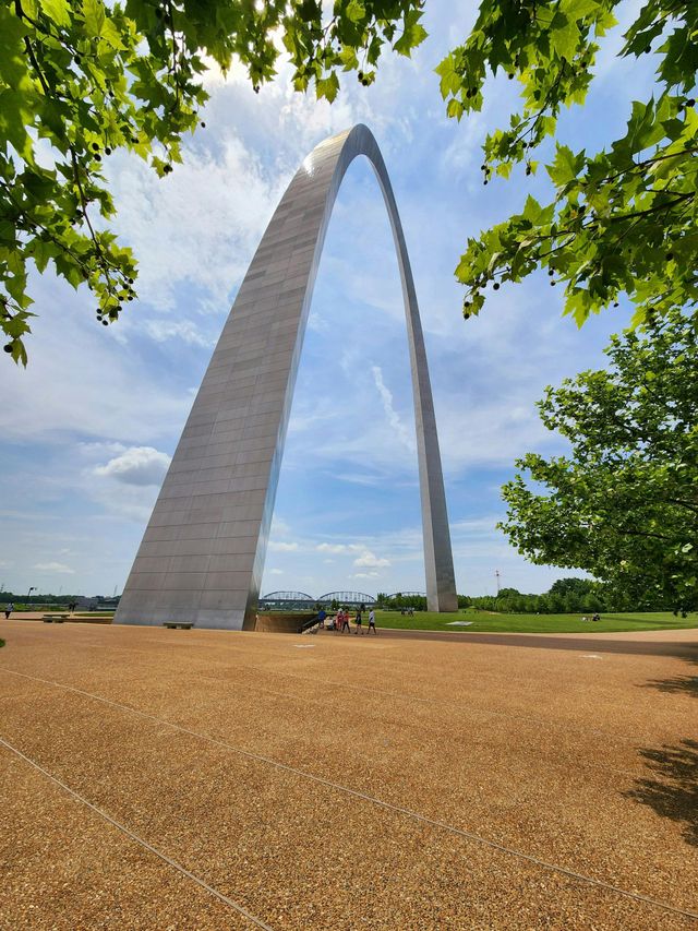 Gateway Arch in St. Louis framed by green trees and a cloudy sky