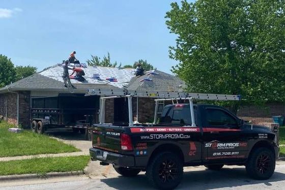 Roofing crew working on a house while a black and red company truck is parked in front.