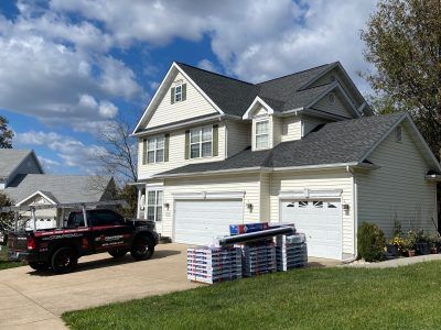 Suburban house with two white garage doors, a black pickup truck, and stacked lumber in the driveway.