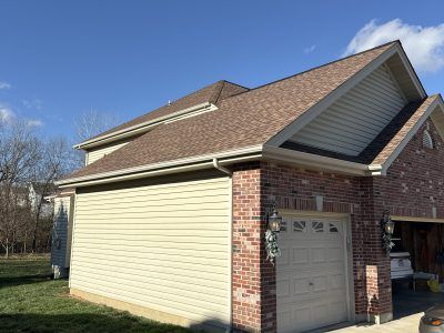Suburban brick garage with beige siding and a single gray door on a sunny day