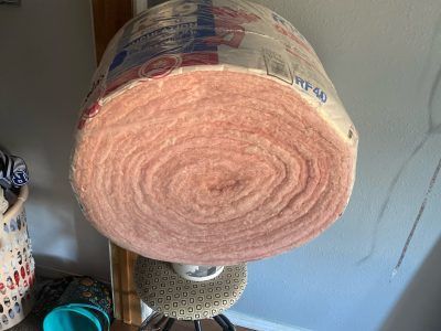 Large roll of pink insulating material with plastic wrapping on a shelf or stand indoors