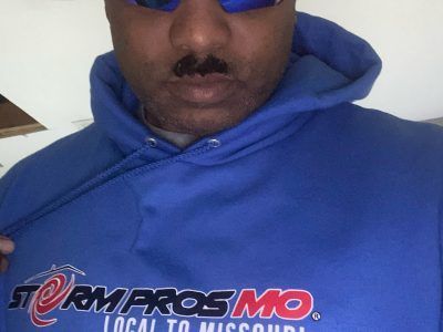 Person in a blue hoodie and sunglasses showing a 