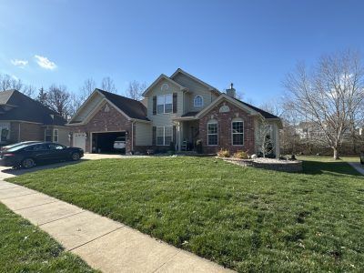 Suburban brick house with attached garage, green lawn, and clear blue sky