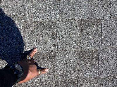 Hand pointing at gray roof shingles with a dark shadow on the left