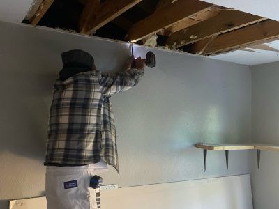 Person drilling into a wall in a basement with exposed ceiling beams.