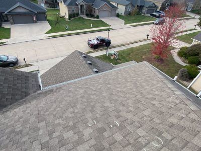 Roof view of a suburban street with houses, parked car, and a small tree with red leaves