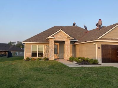 Single-story beige brick house with a front lawn and driveway at dusk