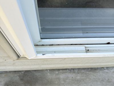 Close-up of a white sliding door track with a gap and worn sill on concrete floor