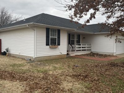 Single-story beige house with dark roof, front porch, and leaf-covered yard