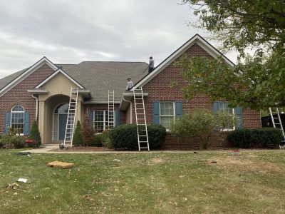 Brick house with two extension ladders on the front roof, under a cloudy sky.