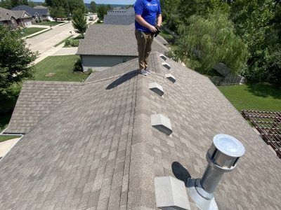 Worker on a shingled roof inspecting roof vents on a sunny residential house