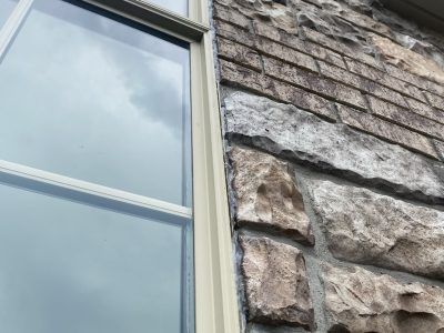 Stone building wall beside a white-trimmed window with blue sky reflected in the glass