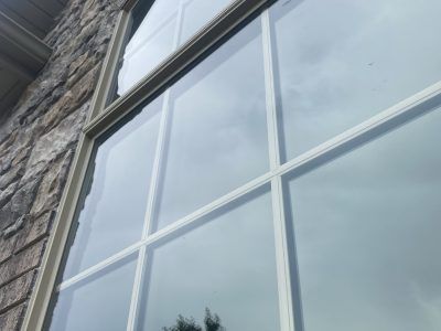 Stone building wall with large white-framed windows reflecting a cloudy sky