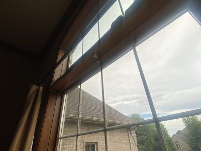 View through a window with wooden blinds to a cloudy sky and rooftops outside.