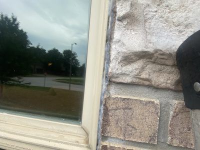 Close-up of a window frame beside a stone wall, reflecting a cloudy street and trees outside