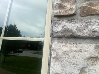 Window beside a stone wall reflecting trees and a cloudy sky