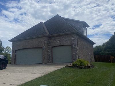 Two-car garage with brick exterior, dark roof, and concrete driveway in a suburban yard