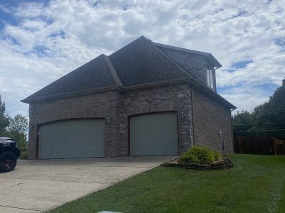 Two-story brick house with a double garage, driveway, and green lawn under a cloudy sky