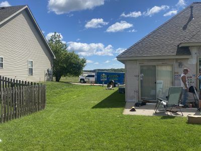 Backyard between two houses, with a person working on a patio beside a sliding door.