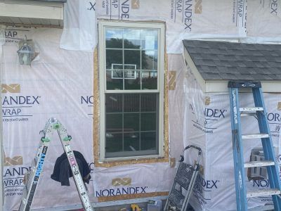 Home exterior under construction with a new door, ladders, and wrapped siding.