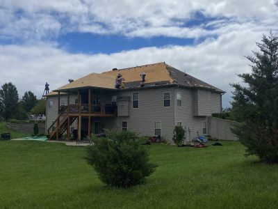 Two-story house with tan roof and gray siding in a grassy yard under a cloudy sky