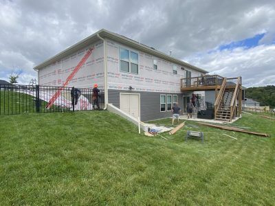 Two-story house under construction with workers, scaffolding, and a grassy yard under cloudy skies
