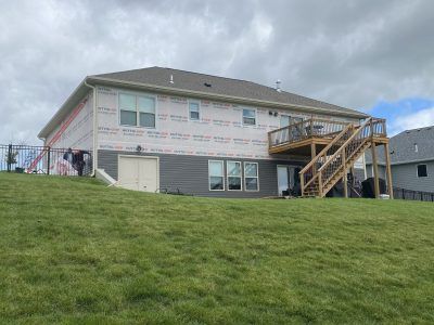 Two-story house with exterior stairs on a grassy hillside under cloudy sky