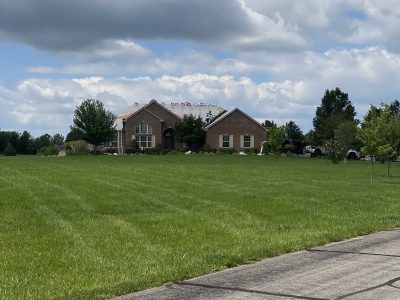 Large brick house on a wide green lawn under a cloudy sky, viewed from a paved road